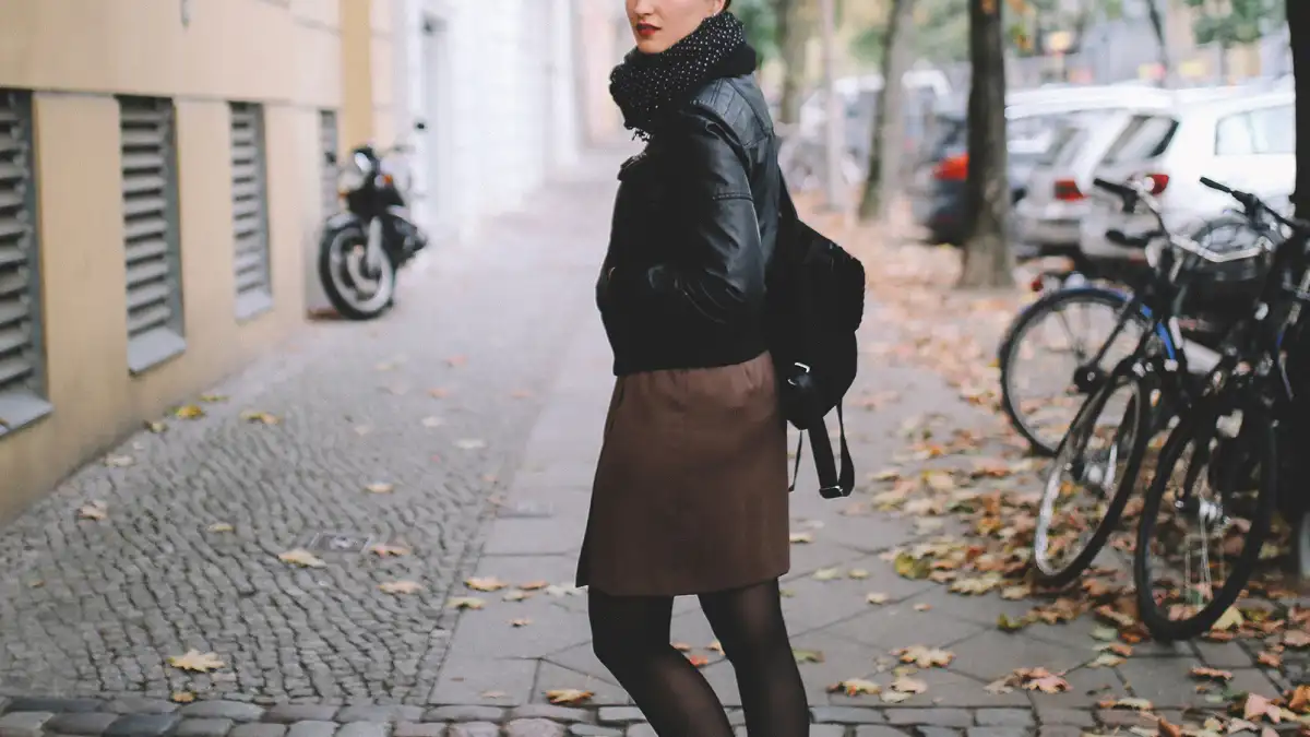 Vintage toned portrait of a young woman in Berlin, wearing a black leather jacket and a beige skirt, walking on the streets of Prenzlauer Berg, near Mitte in the late Autumn day. Street style, casual fashion concept.