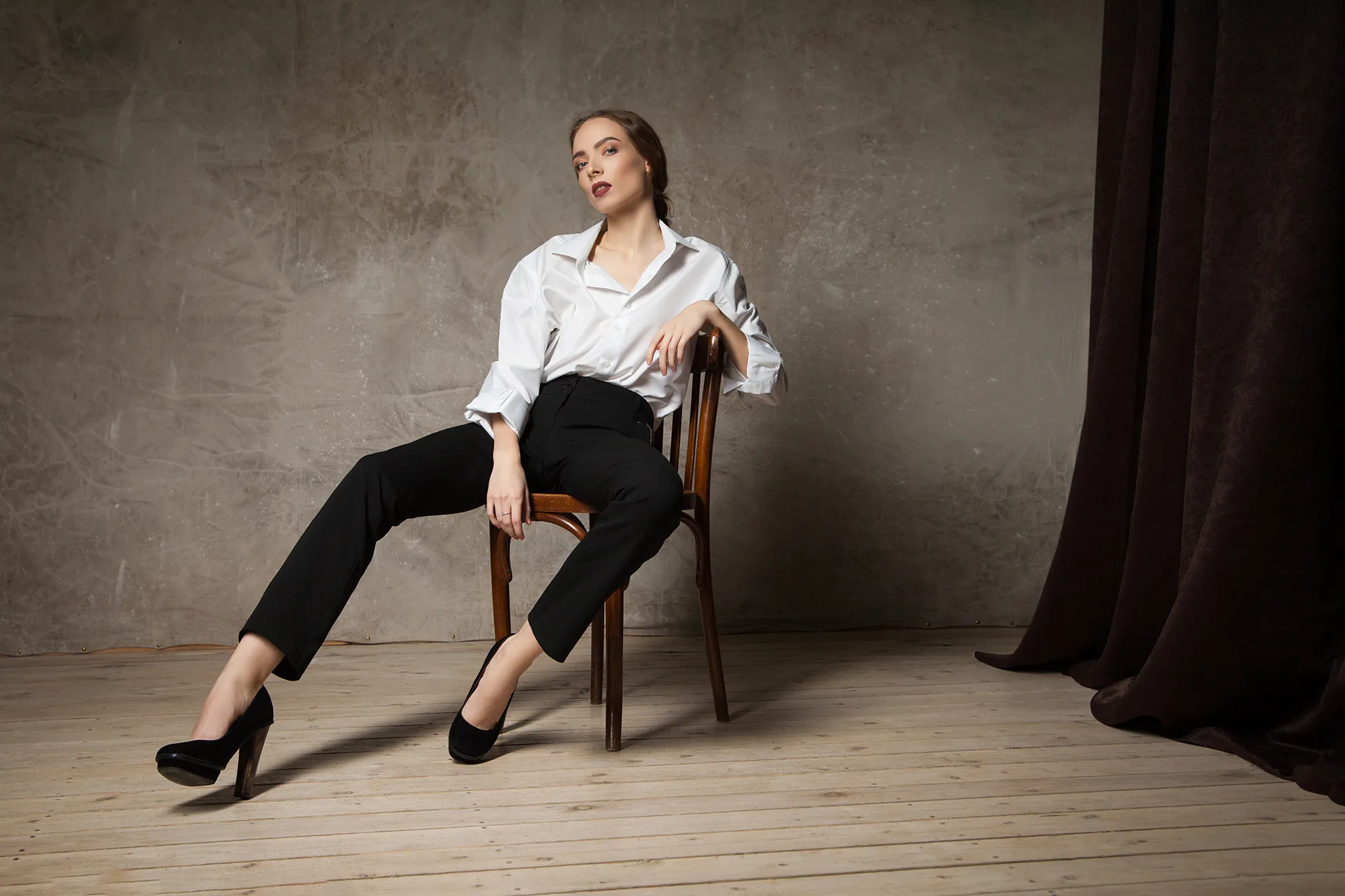 Stylish young attractive woman looking at camera and posing on chair in studio.