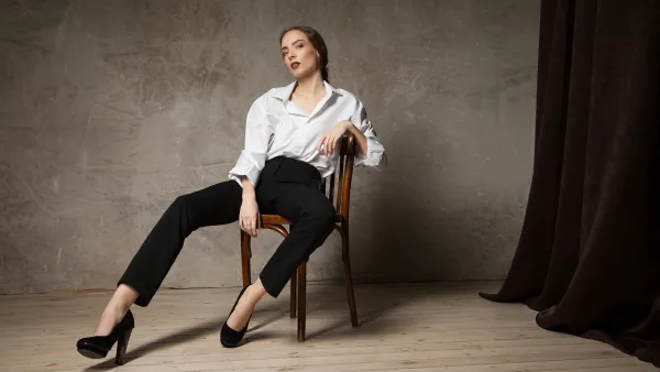 Stylish young attractive woman looking at camera and posing on chair in studio.