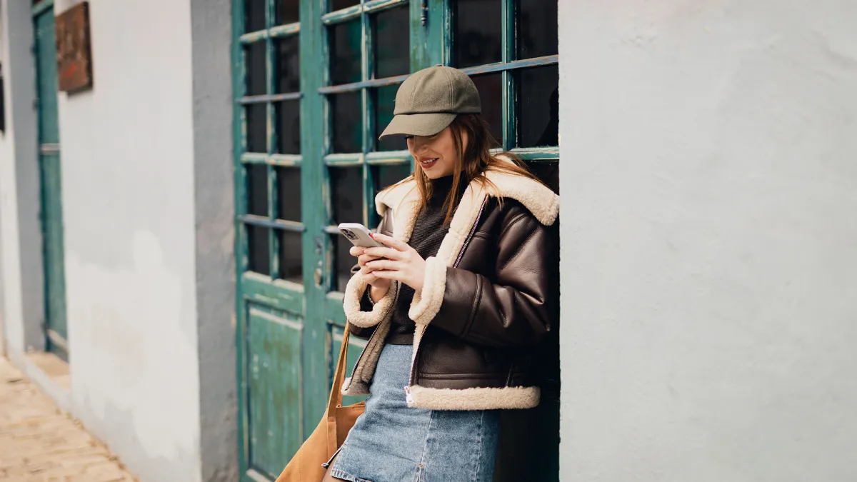 Smiling young woman using a smartphone in the city street on a lovely autumn day