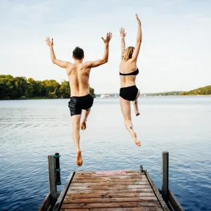 Happy couple jumping into the water from a jetty