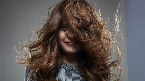studio shot of a young female brunette in front of a gray background, wearing a gray outfit . her face half hidden behind her hair