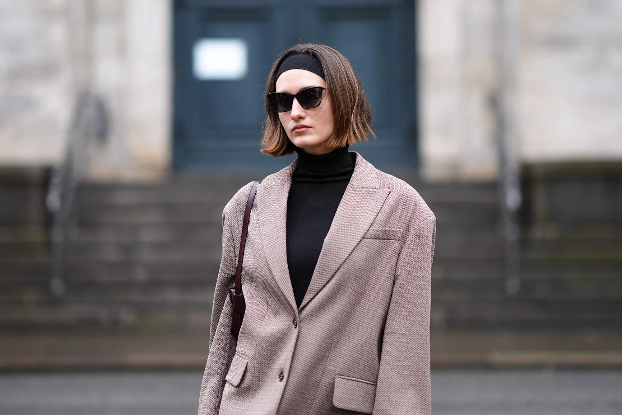 A guest wears a headband, sunglasses, a black turtleneck pullover , a beige oversized blazer jacket , outside Aeron, during the Copenhagen Fashion Week AW24 on January 30, 2024 in Copenhagen, Denmark. (Photo by Edward Berthelot/Getty Images)