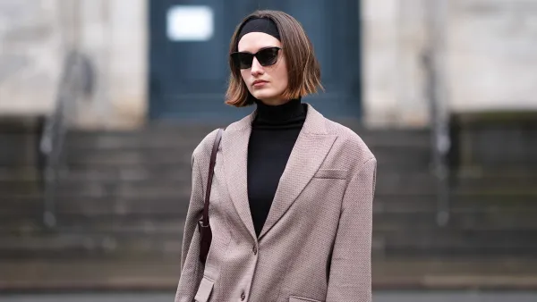 A guest wears a headband, sunglasses, a black turtleneck pullover , a beige oversized blazer jacket , outside Aeron, during the Copenhagen Fashion Week AW24 on January 30, 2024 in Copenhagen, Denmark. (Photo by Edward Berthelot/Getty Images)