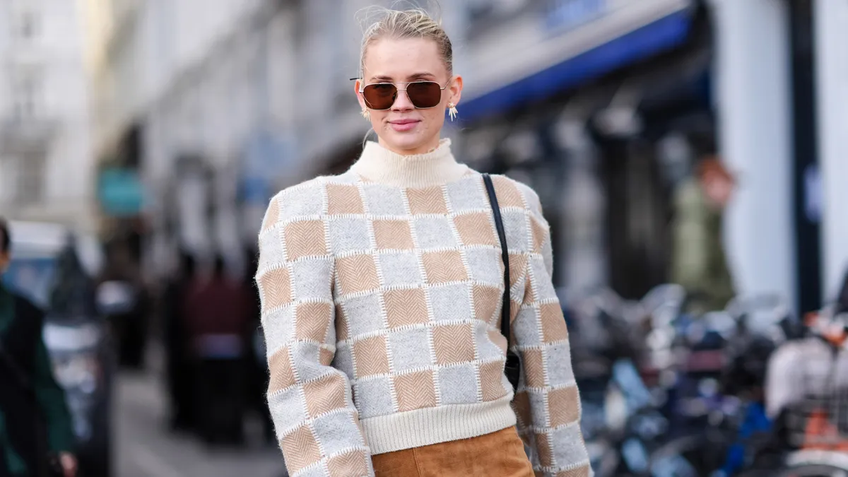A guest wears sunglasses, a white and beige checkered / checked pattern printed turtleneck ribbed wool pullover with shoulder pads, a beige / brown suede mini skirt , outside Mark Kenly Domino Tan, during the Copenhagen Fashion Week AW24 on February 01, 2024 in Copenhagen, Denmark. (Photo by Edward Berthelot/Getty Images)