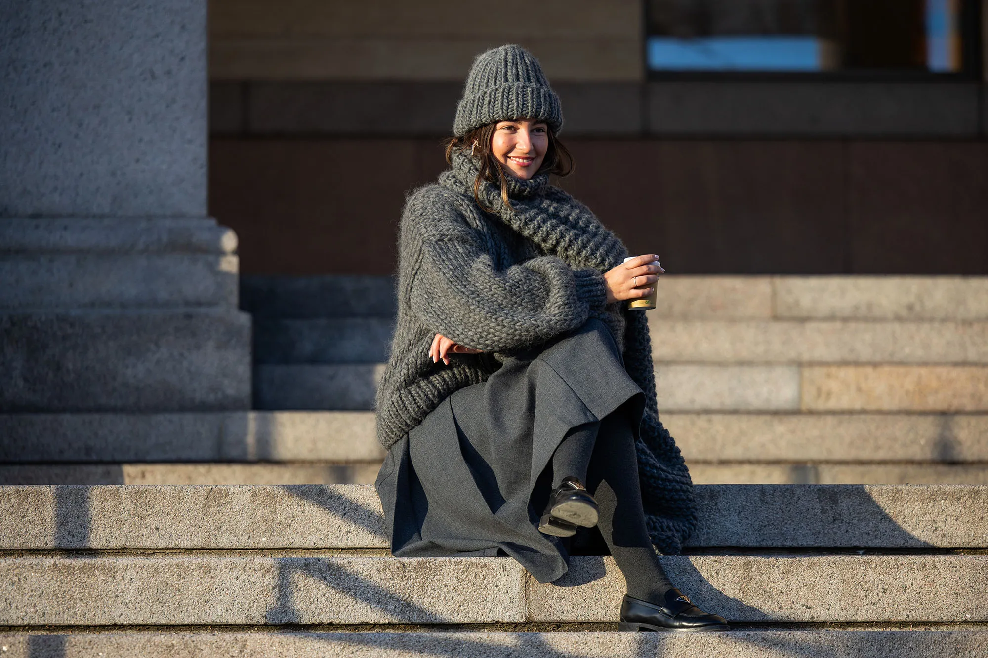 Inspiration: Benthe Liem sitting drinking coffee wears grey beanie, knit, scarf, skirt, black Prada bag outside Marimekko during the Copenhagen Fashion Week AW24 on February 01, 2024 in Copenhagen, Denmark. (Photo by Christian Vierig/Getty Images)