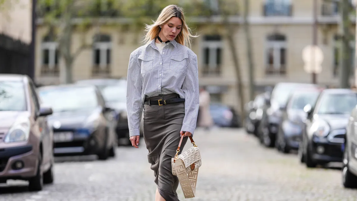 PARIS, FRANCE - APRIL 15: Natalia Verza wears diamonds earrings, a white with small black striped print pattern shirt, a white latte matte leather with cut-out FF monogram pattern crossbody bag from Fendi, a black shiny leather small belt, a dark gray long slit / split skirt, white platform soles ankle boots , during a street style fashion photo session, on April 15, 2023 in Paris, France. (Photo by Edward Berthelot/Getty Images)