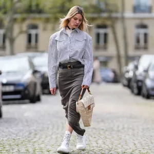 PARIS, FRANCE - APRIL 15: Natalia Verza wears diamonds earrings, a white with small black striped print pattern shirt, a white latte matte leather with cut-out FF monogram pattern crossbody bag from Fendi, a black shiny leather small belt, a dark gray long slit / split skirt, white platform soles ankle boots , during a street style fashion photo session, on April 15, 2023 in Paris, France. (Photo by Edward Berthelot/Getty Images)