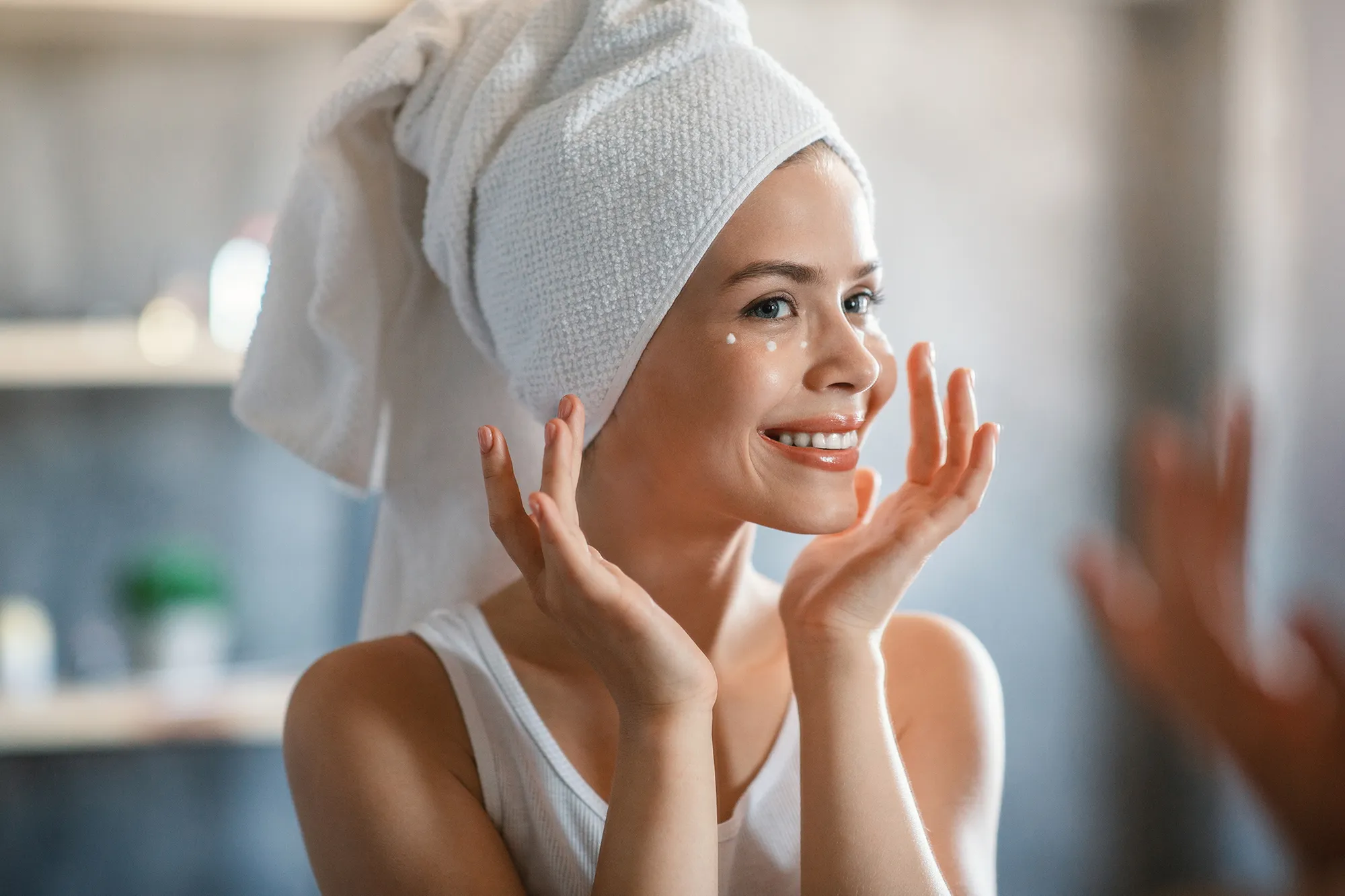 Lovely lady applying cream under her eyes after shower near mirror at home