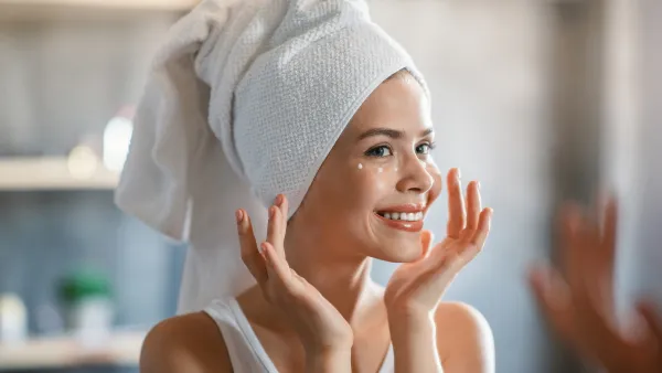 Lovely lady applying cream under her eyes after shower near mirror at home