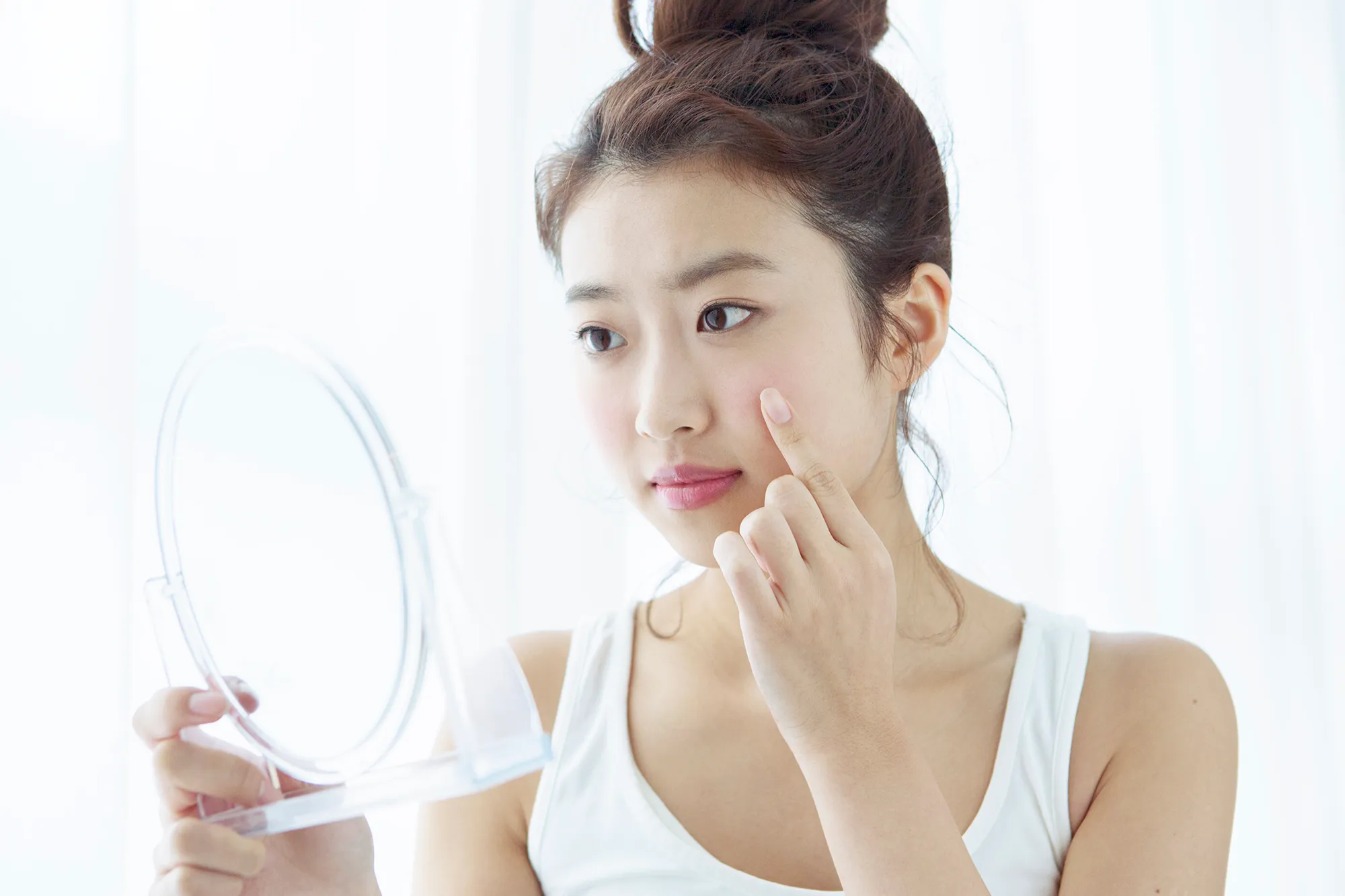 Young woman looking at her cheek in hand mirror
