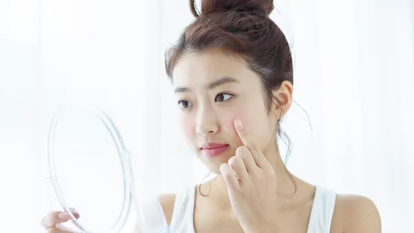 Young woman looking at her cheek in hand mirror