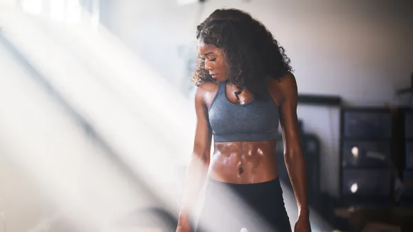 Muscular woman sweating from work out in home gym with light rays