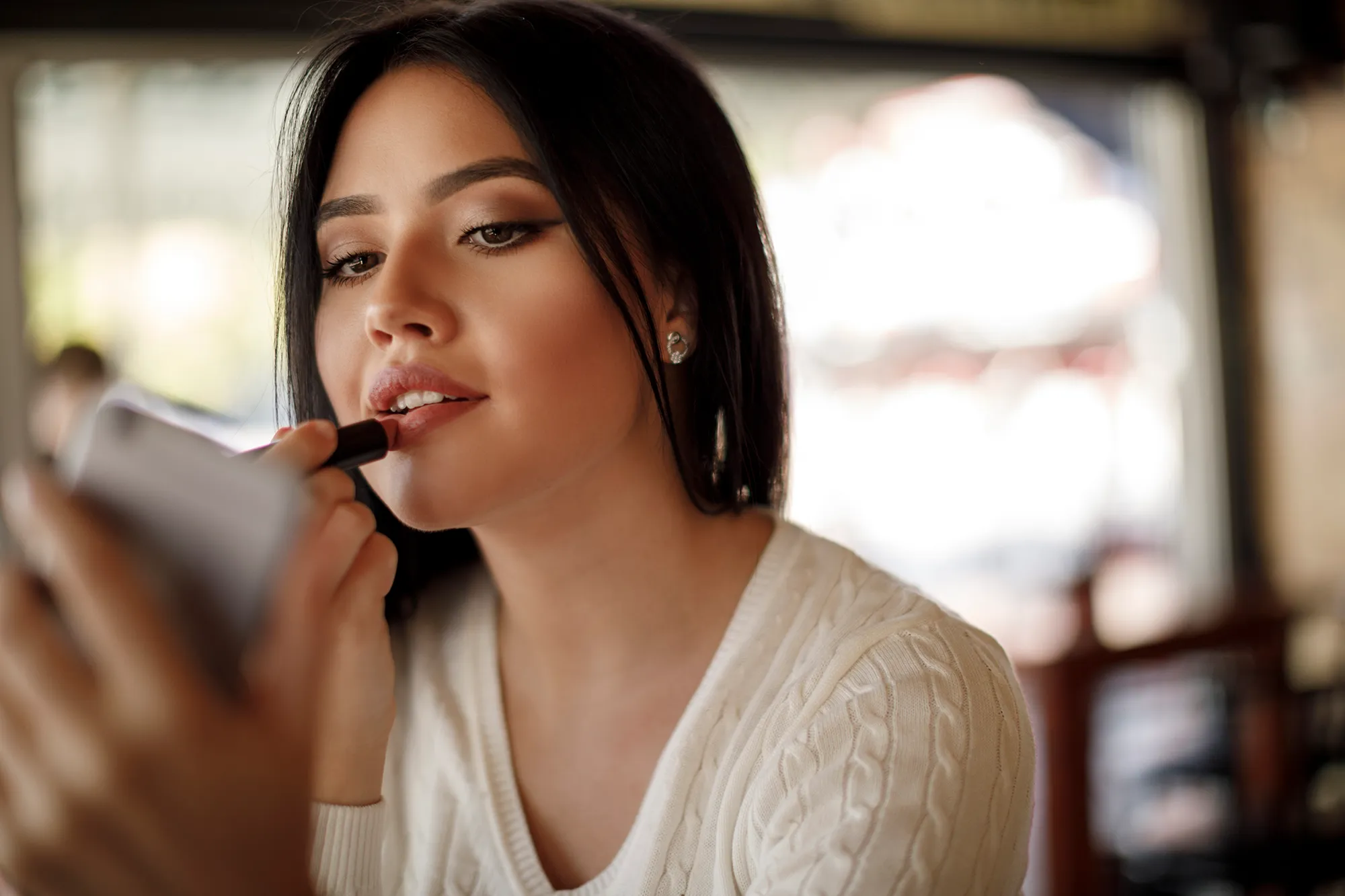 Young woman applying lipstick at a cafe