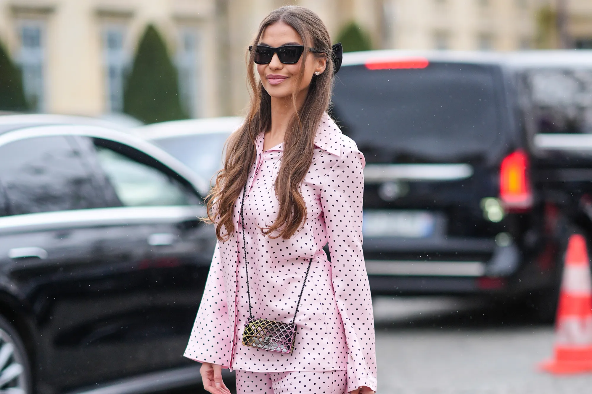 A guest wears sunglasses, a pink Chanel pajama with flared pants and printed polka dots, a Chanel bag, platform shoes, outside Chanel, during the Womenswear Fall/Winter 2024/2025 as part of Paris Fashion Week on March 05, 2024 in Paris, France.
