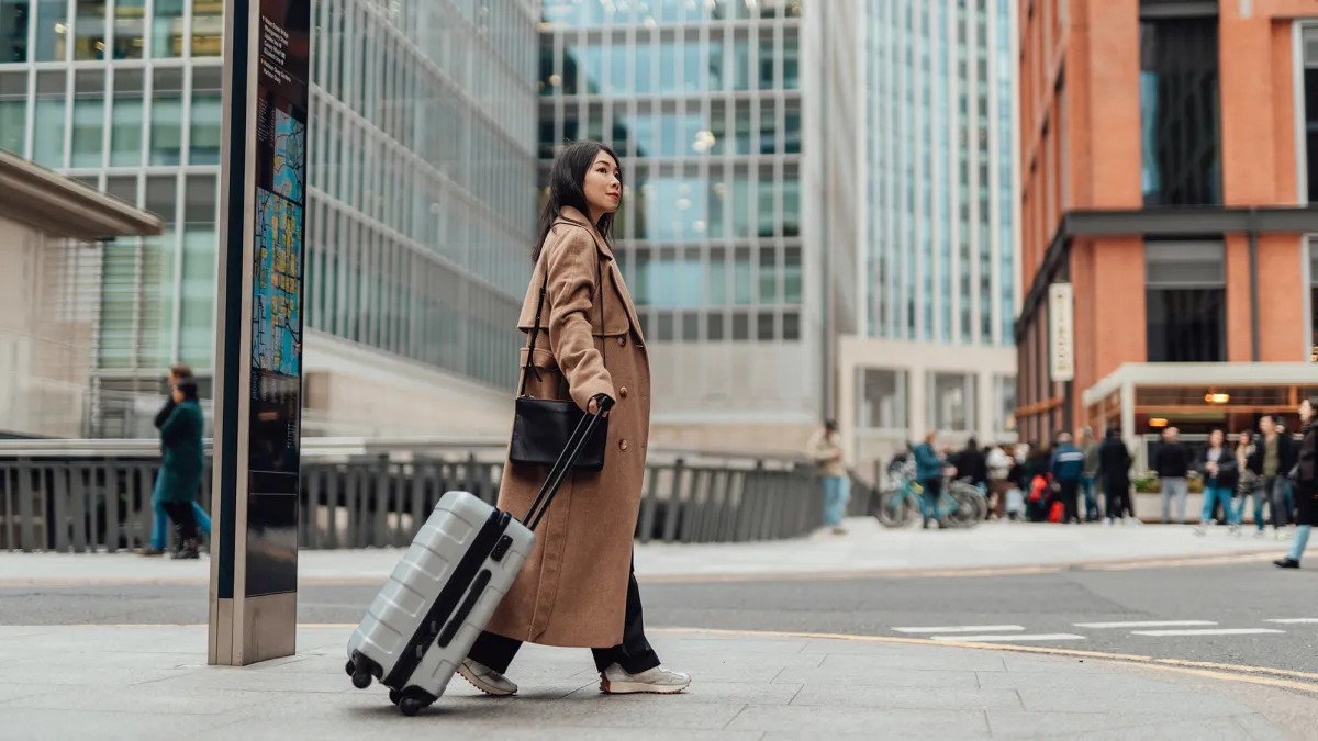 Young businesswoman carrying luggage, walking on the high street in the city.