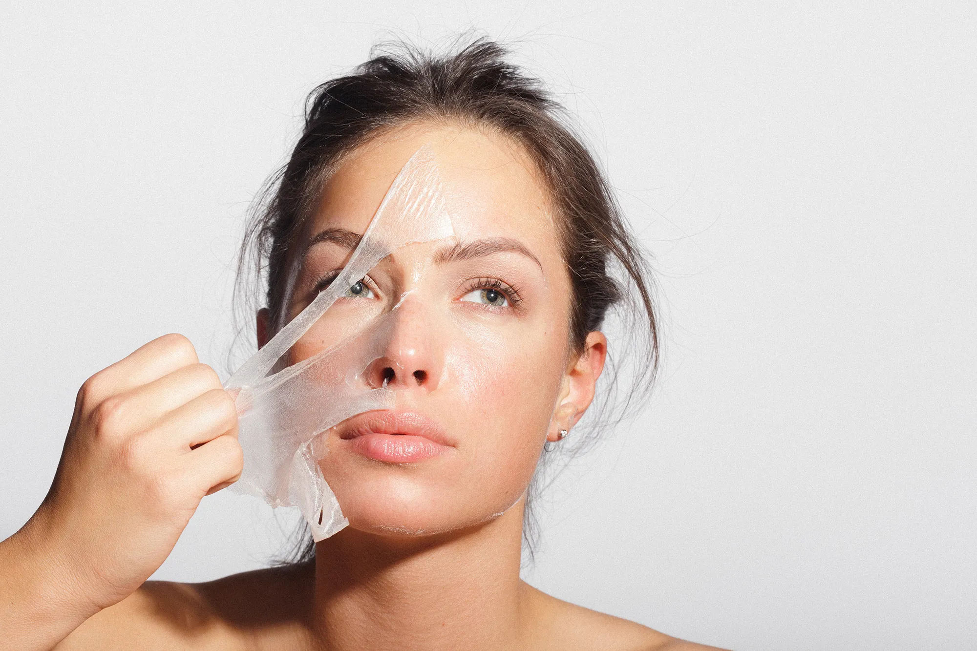 Close-up beauty portrait of a beautiful, natural young woman removing face mask.