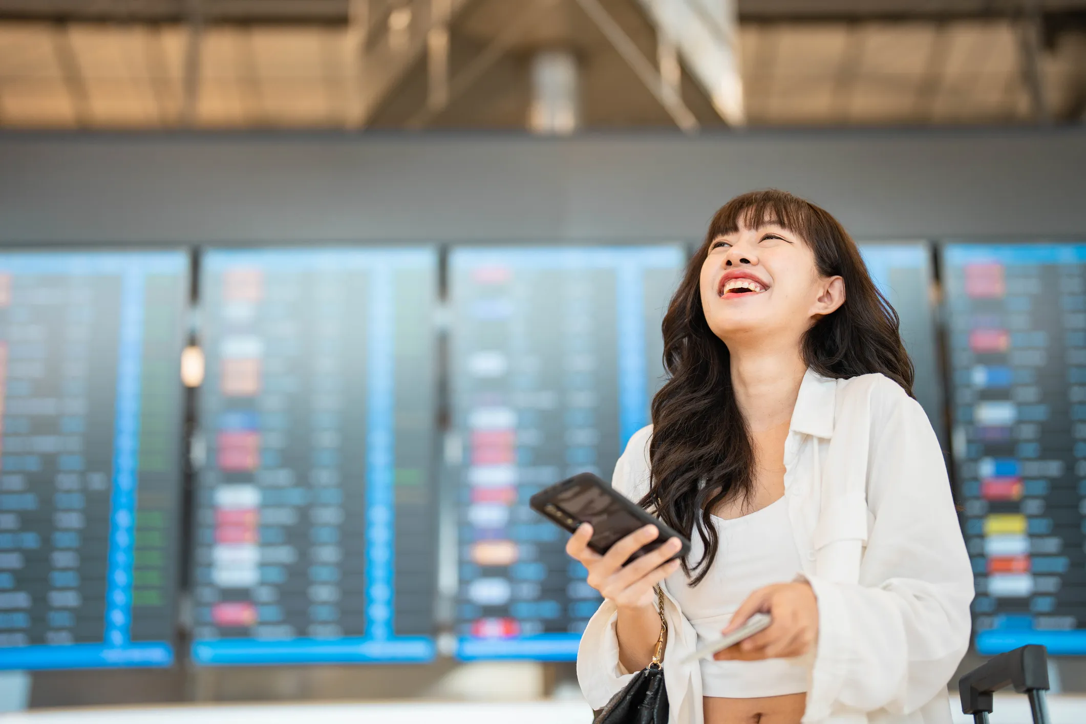 Smiling young woman text messaging on smartphone while waiting for her flight in airport lounge