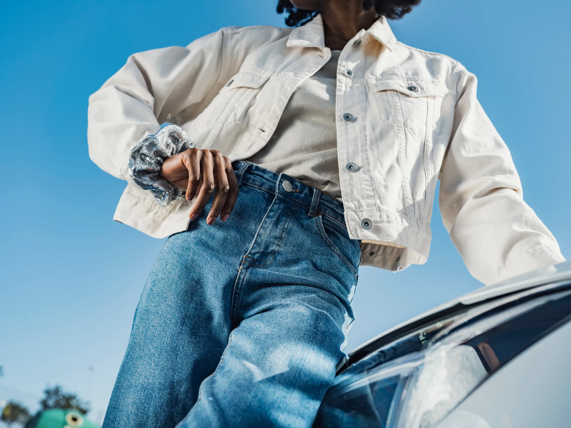 Young woman leaning on car headlight in front of sky