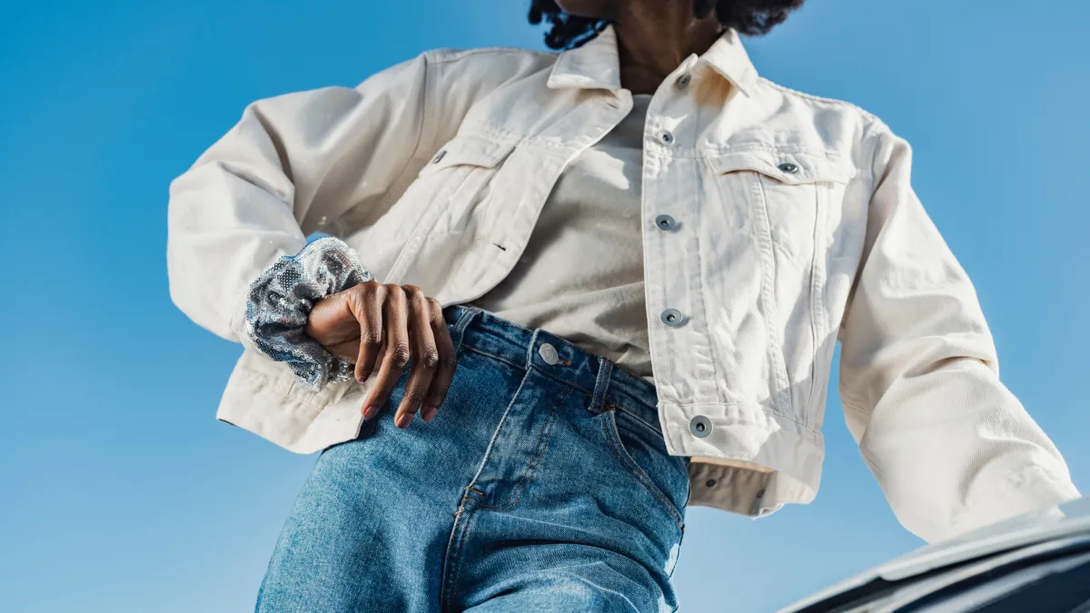 Young woman leaning on car headlight in front of sky