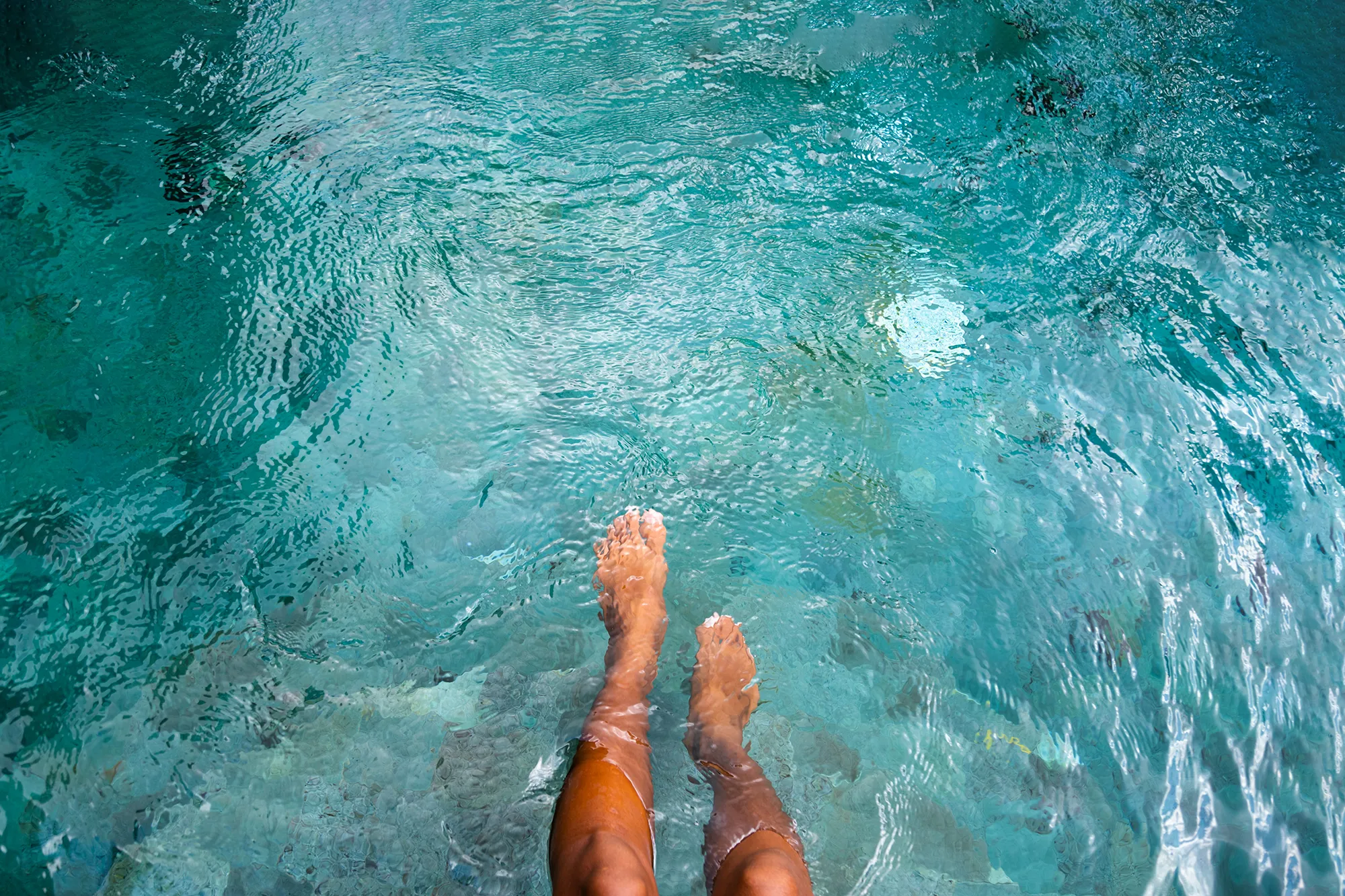 Top view of woman playing with water with legs and feet in swimming pool. Copy space. Vacation and summertime concepts.