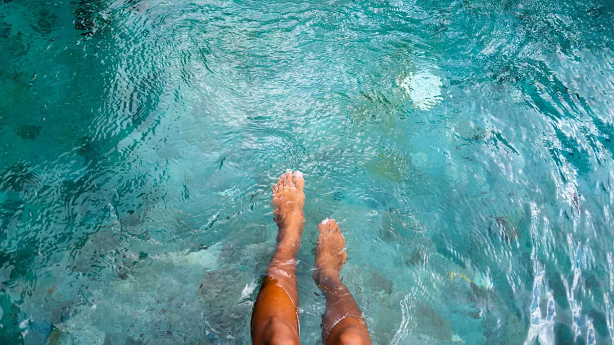 Top view of woman playing with water with legs and feet in swimming pool. Copy space. Vacation and summertime concepts.