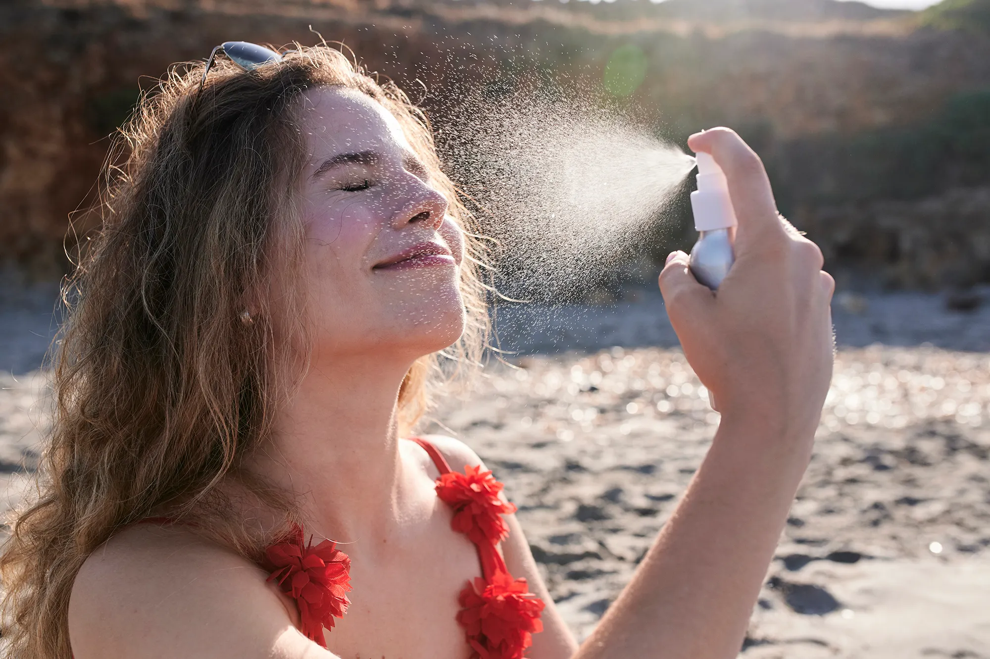 Young woman applying suncream spray on the beach