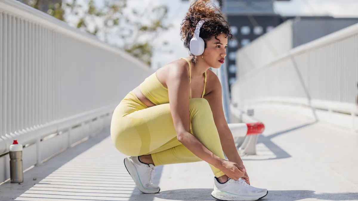 A young woman with wireless headphones tying shoelaces on her trainers before running