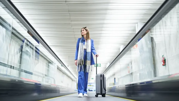 Low angle view of cheerful woman standing in the airport moving walkway with her travel suitcase and looking away. Travel concept.