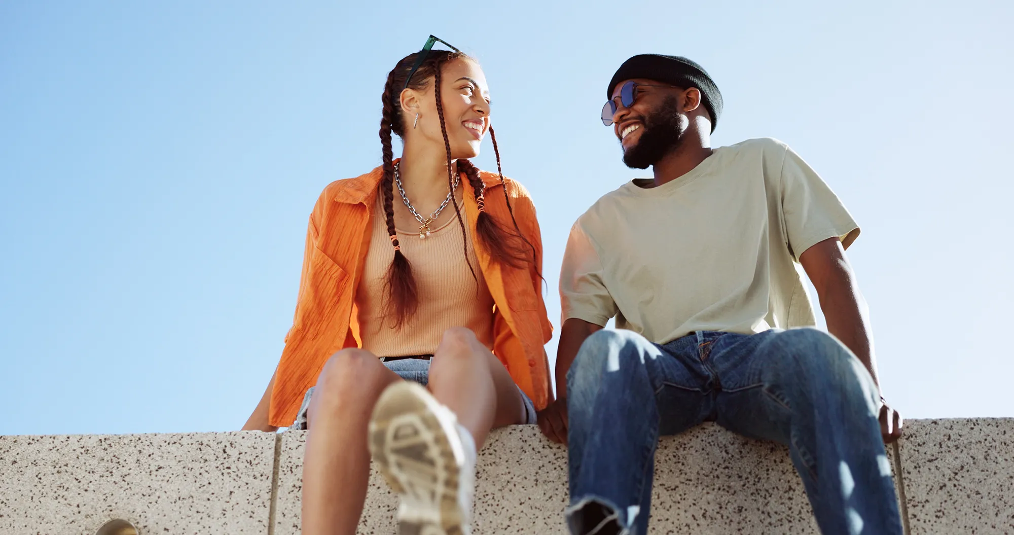 Couple sitting on a wall outdoor against a clear blue sky together