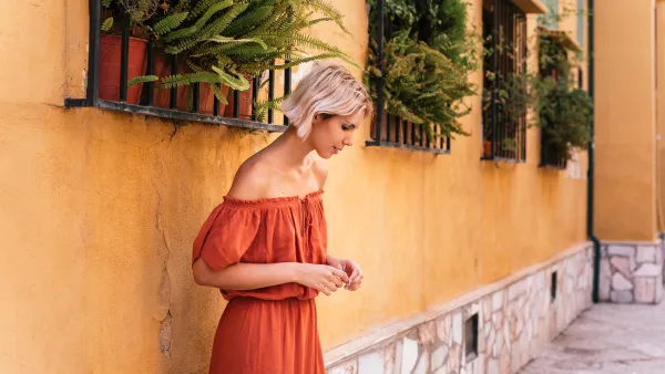Portrait of woman in orange dress near yellow wall with windows with green pots in Granada, Spain