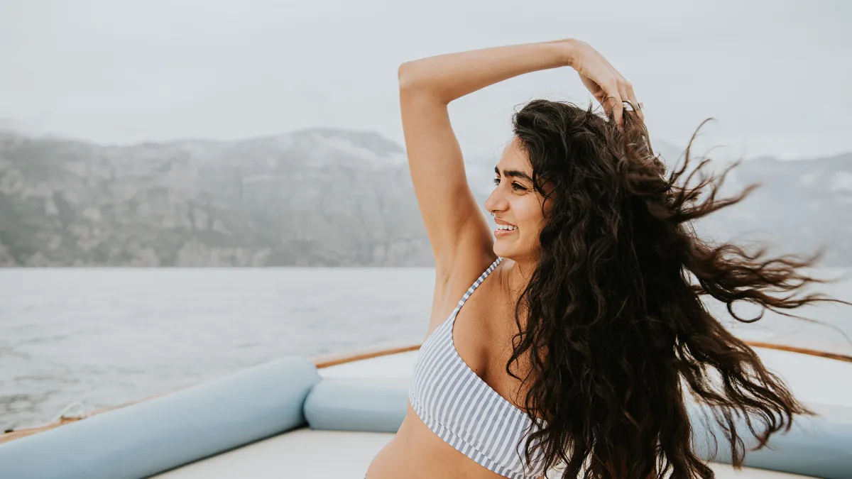 A beautiful young Indian woman enjoys a boat ride. She runs her fingers through her long, thick, wavy hair, which blows in the breeze. She looks away.