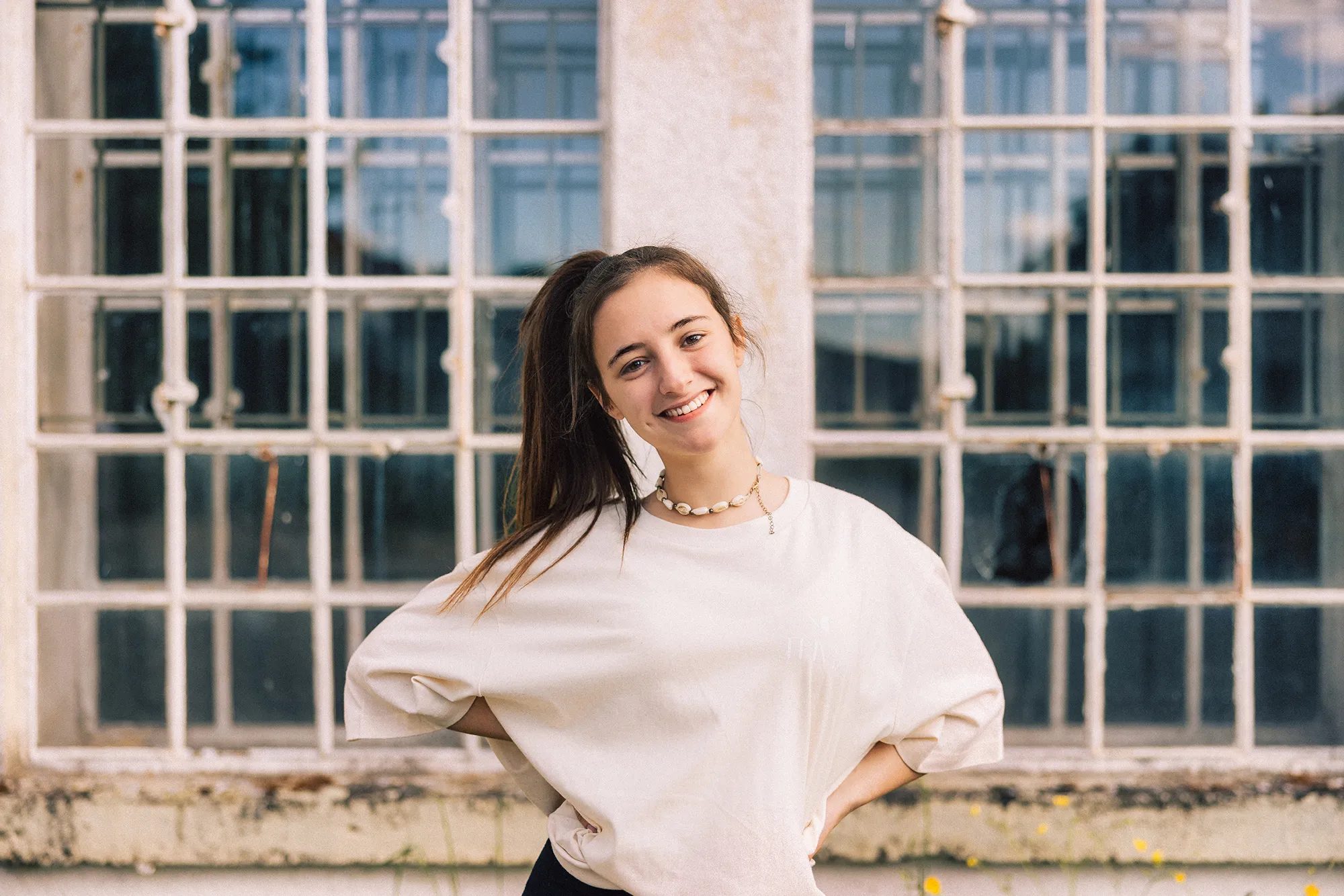 Young fashionable woman with ponytail wearing property released handmade craft designer T-Shirt Standing looking towards the Camera. Majestic industrial Window in the background. Millennial Generation Girl Young Fashion Design Portrait.