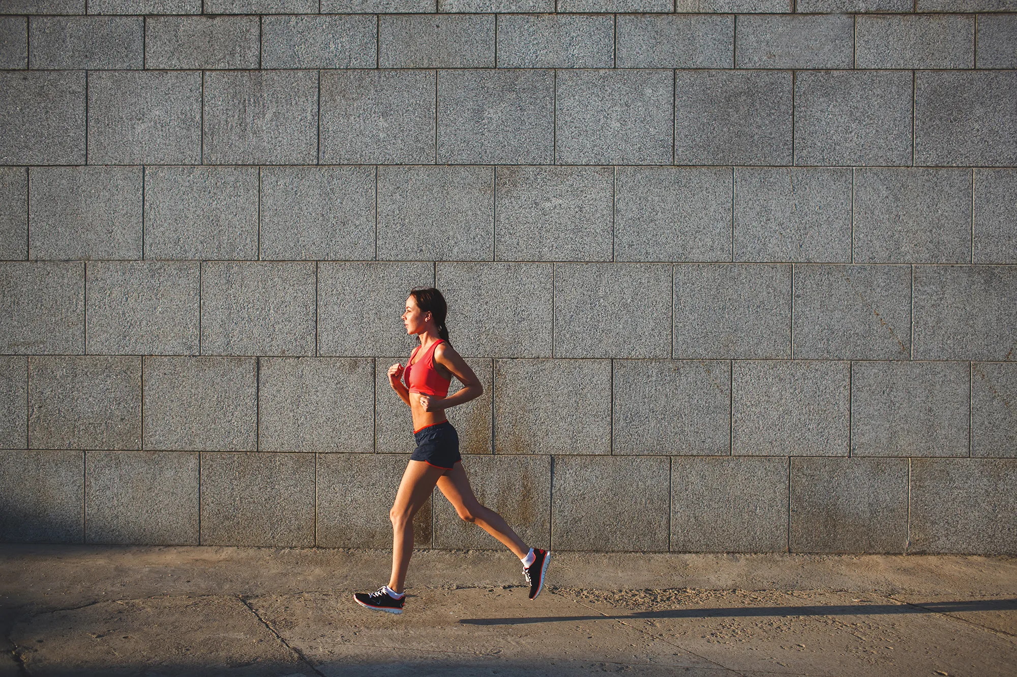 woman working out in an urban setting, running along stone wall
