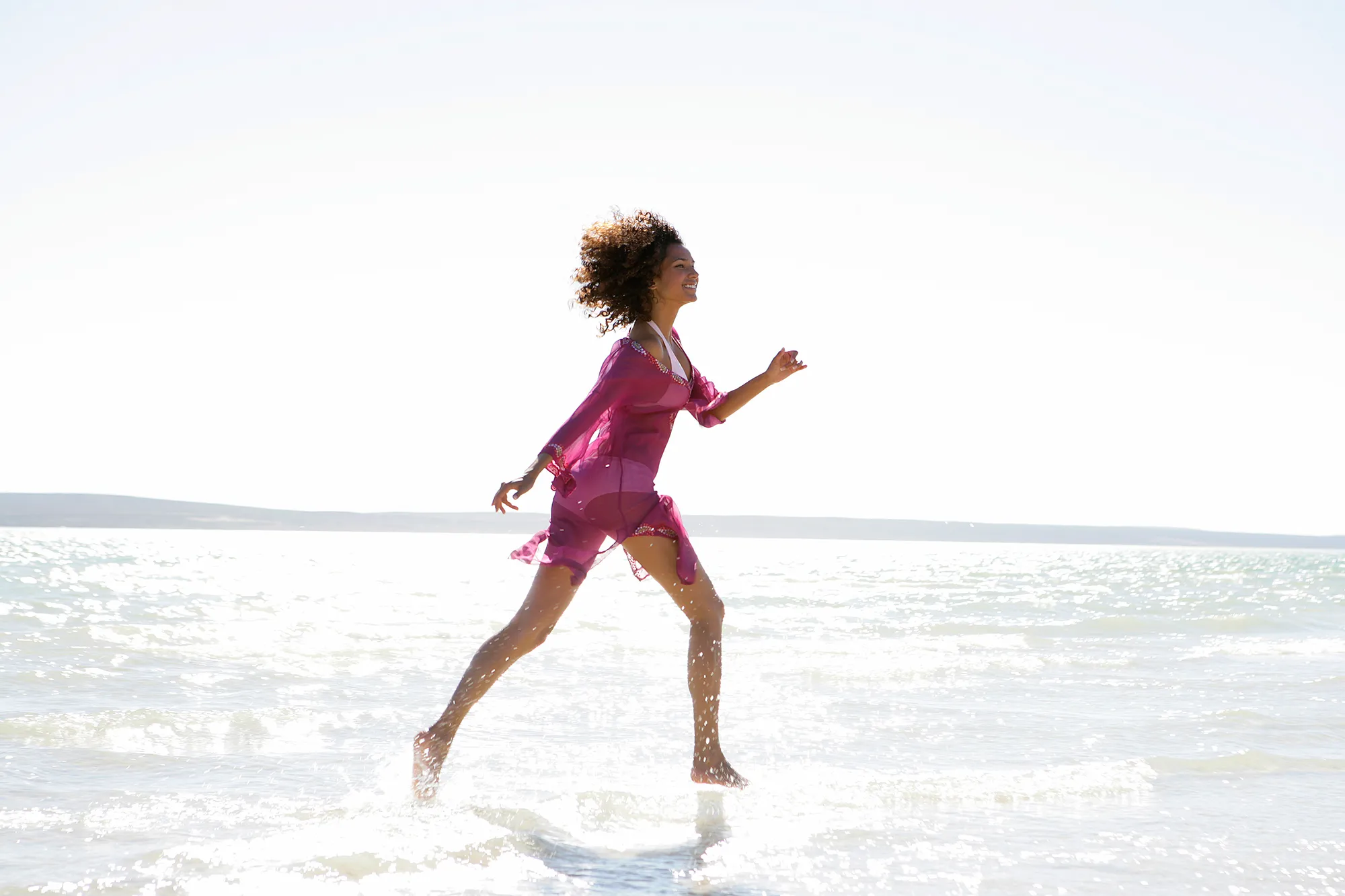 Woman in bikini and cover-up running in ocean