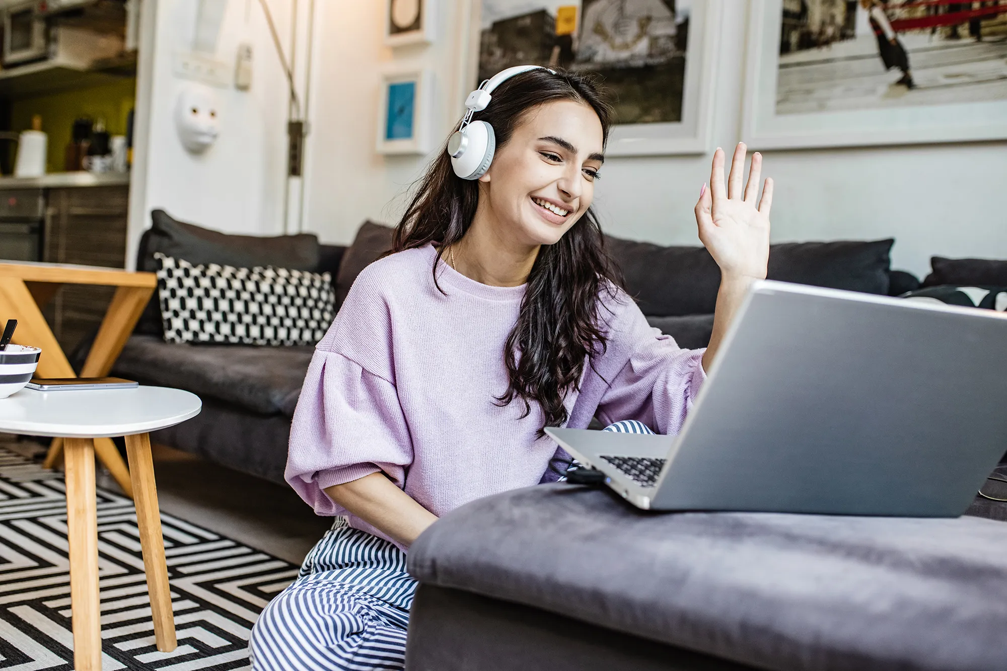 Young woman is at home, having a video call and waving at camera
