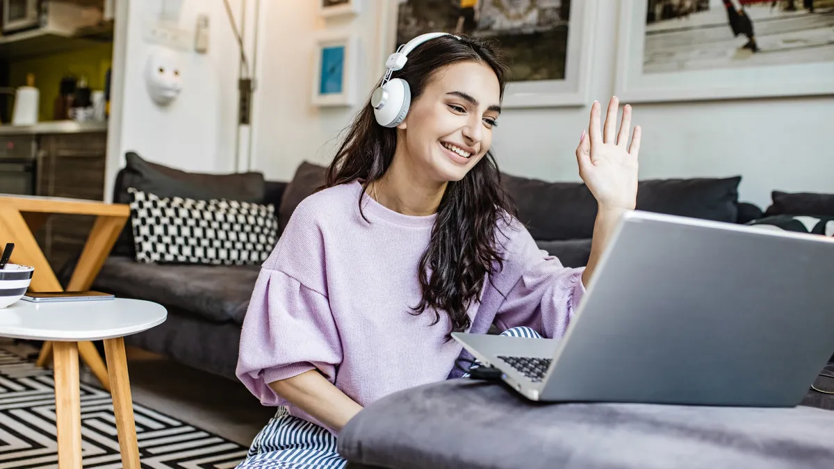 Young woman is at home, having a video call and waving at camera