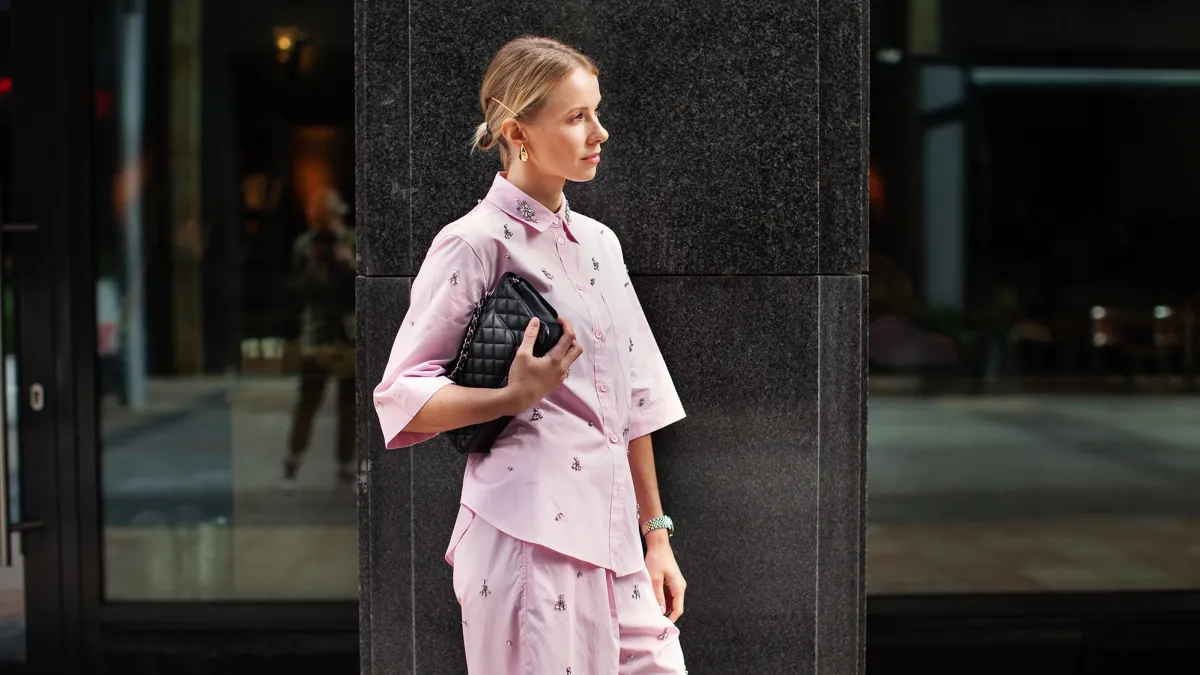 Stylish fashion woman wearing pink suit, shirt and shorts, standing confidently against a city backdrop. Urban street style allure.