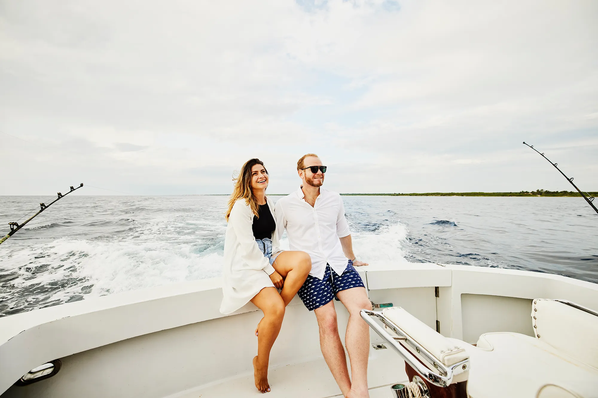 Wide shot of smiling couple sitting on stern of sport fishing boat
