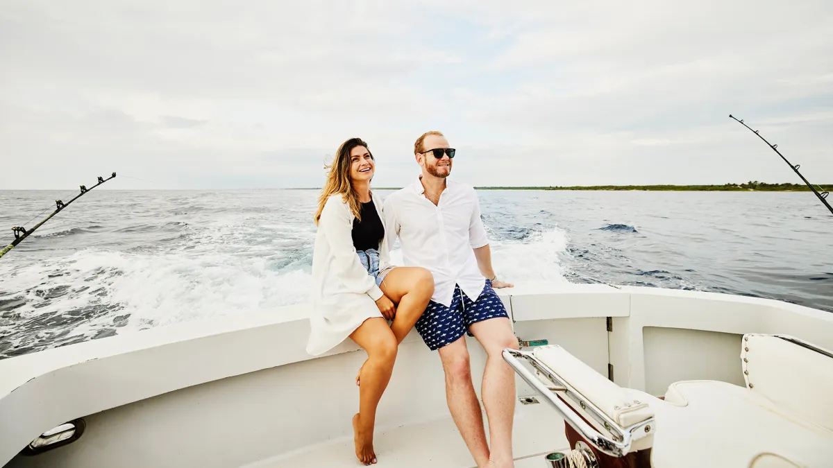 Wide shot of smiling couple sitting on stern of sport fishing boat