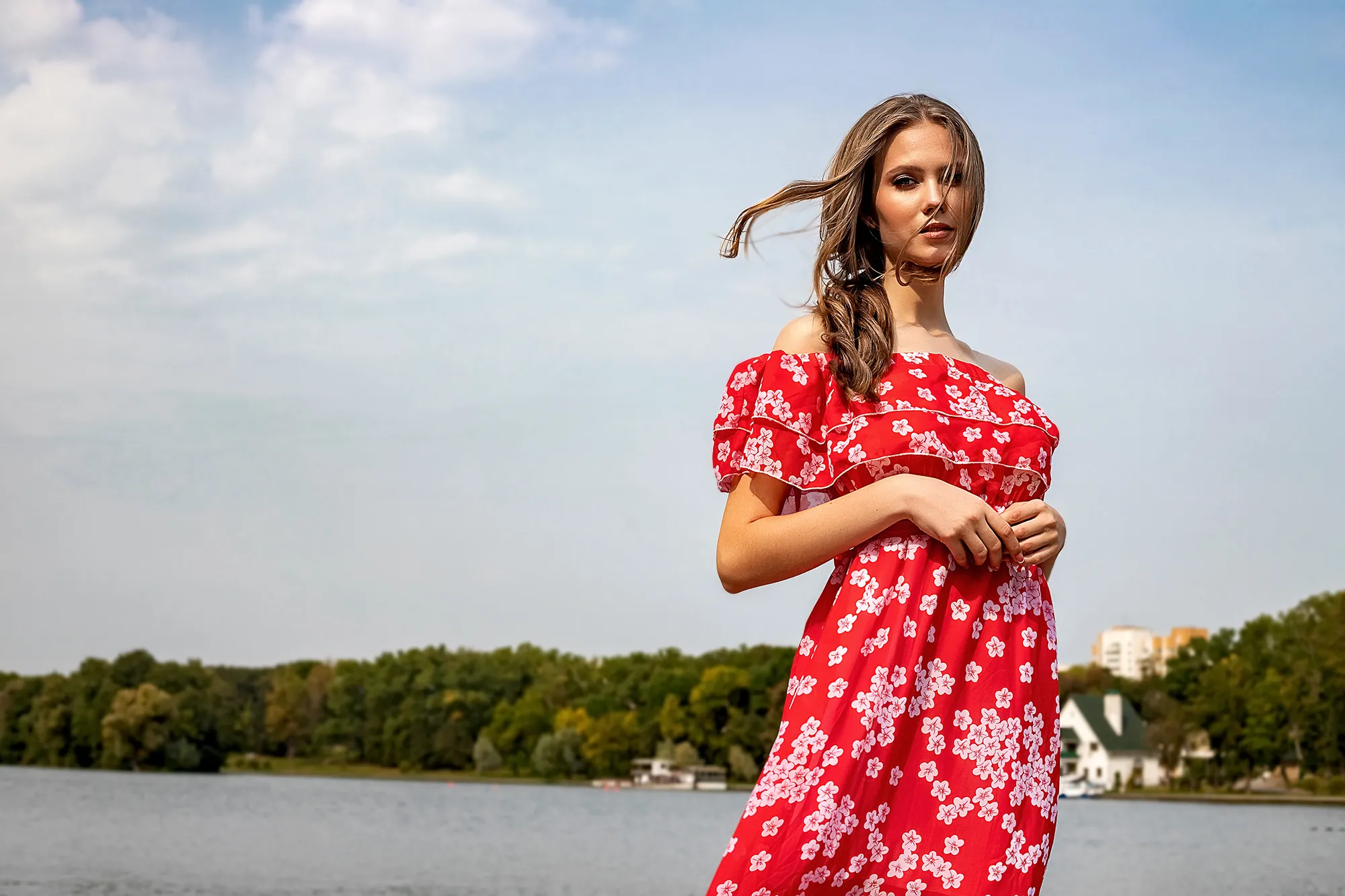 Portrait of a beautiful young brown-haired girl with long hair in a red dress on a lake background. Belarus