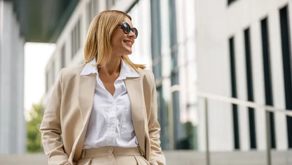 Smiling woman office worker is standing on modern building background and looking at side