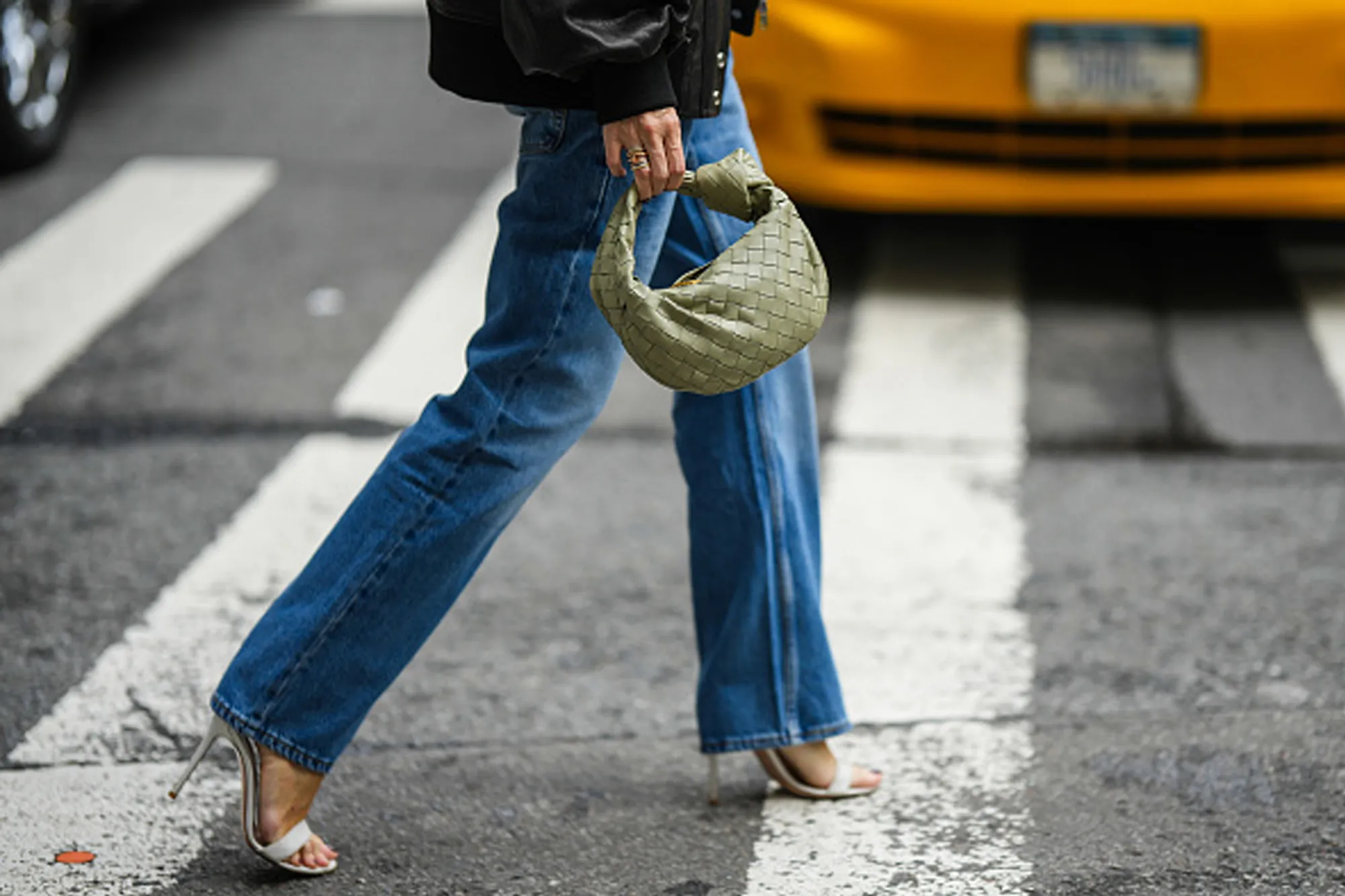 woman wearing jeans, heels and purse walking across street