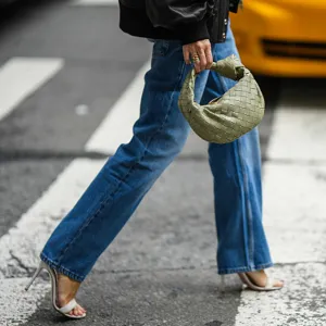 woman wearing jeans, heels and purse walking across street