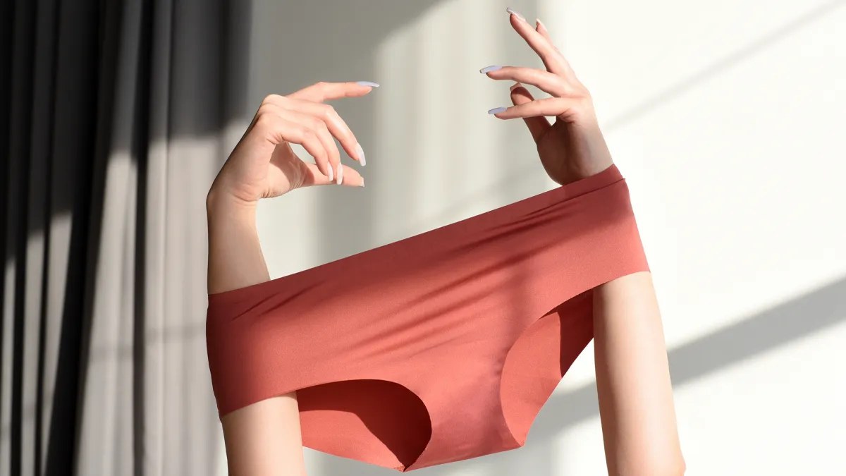 Seamless female panties in the hands of the girl. White background with sun shadow.