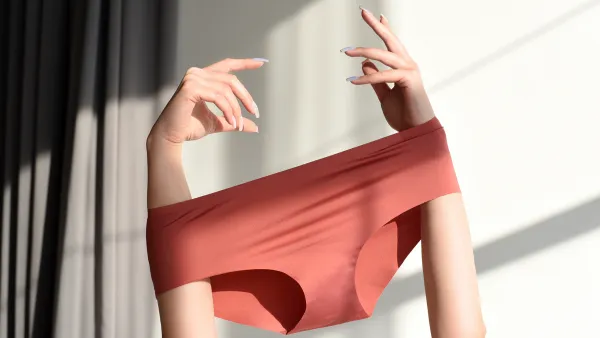 Seamless female panties in the hands of the girl. White background with sun shadow.