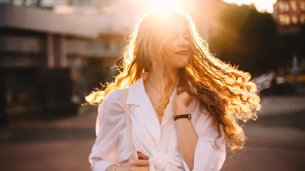 Portrait of happy successful woman with tousled hair in city at sunset