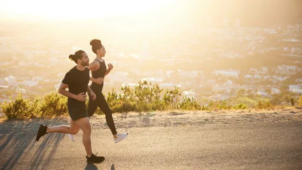 Two fit young friends in sportswear jogging together along a scenic road overlooking the city on a sunny afternoon
