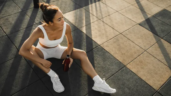 Sportive woman with slim tanned body relaxing after fitness training on outdoors sports ground. Taking a break to drink cold water and refresh. Sports hobby, healthy and active lifestyle concept.