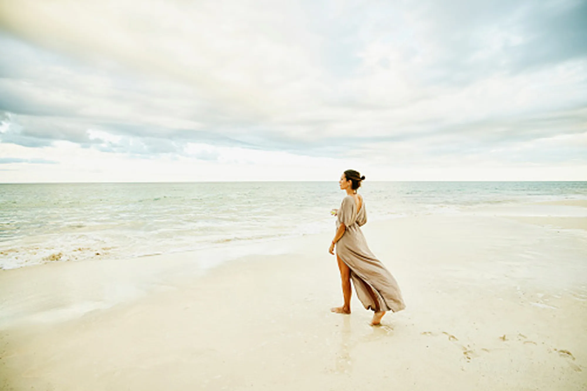 woman walking on beach in beige dress